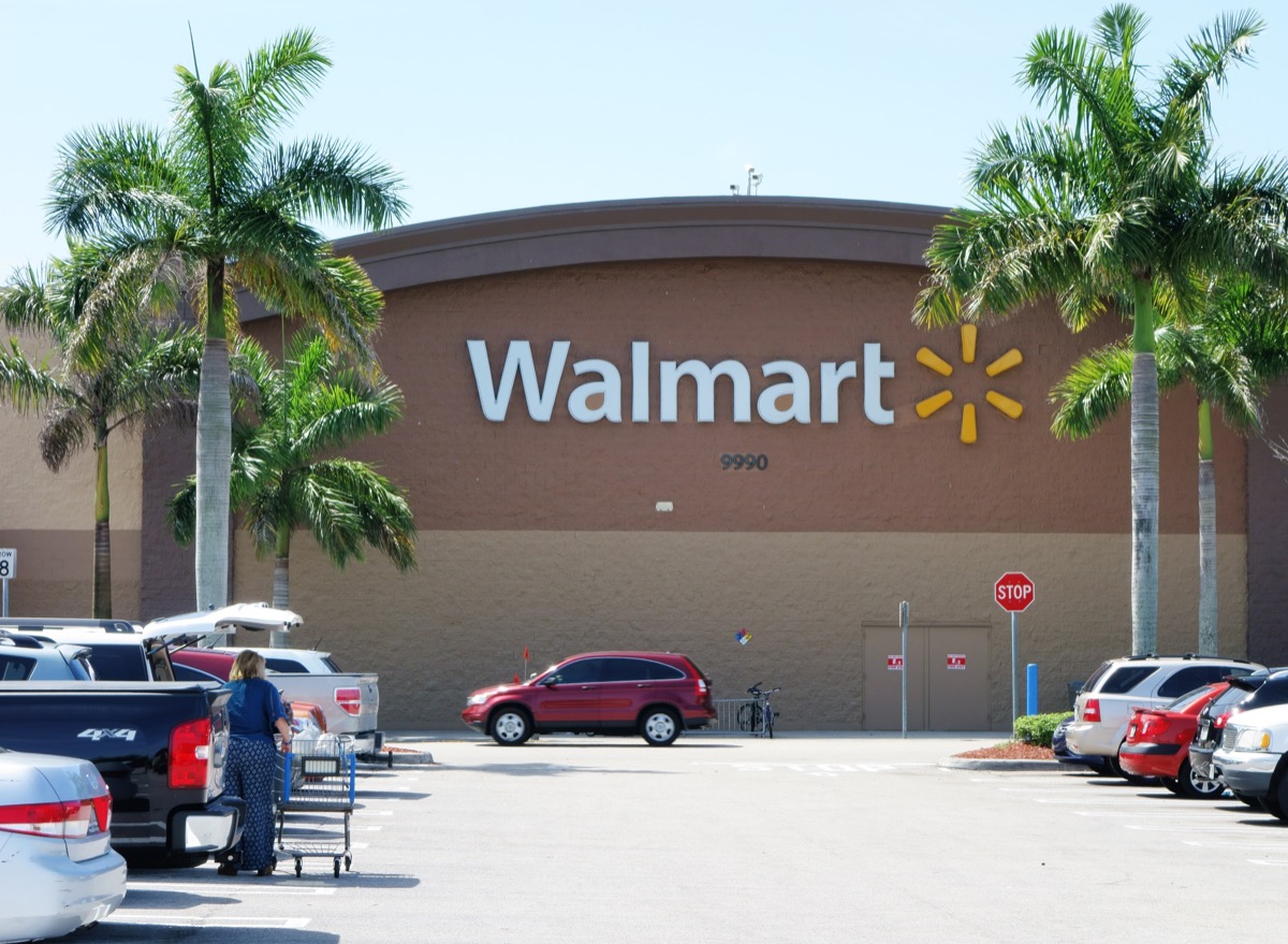  Ein Walmart-Laden mit vollem Parkplatz. Walmart ist der größte Einzelhändler der Welt und betreibt Tausende von großen Discount-Kaufhäusern. Eine Kundin leert ihren Einkaufswagen auf dem Parkplatz in ein Auto.