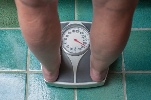 Person weighing themselves on scale because of weight loss