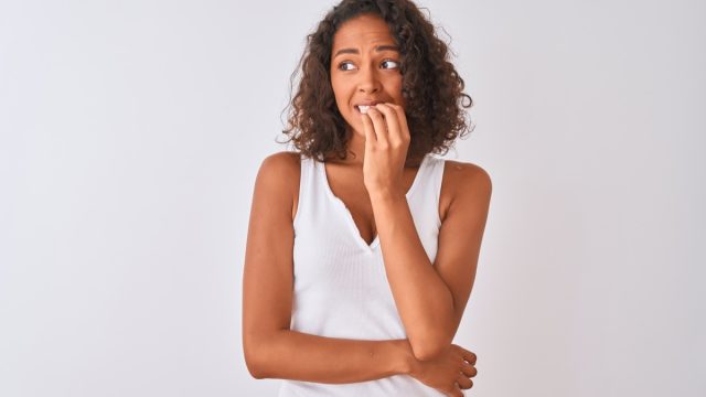 Young brazilian woman wearing casual t-shirt standing over isolated white background looking stressed and nervous with hands on mouth biting nails. Anxiety problem.