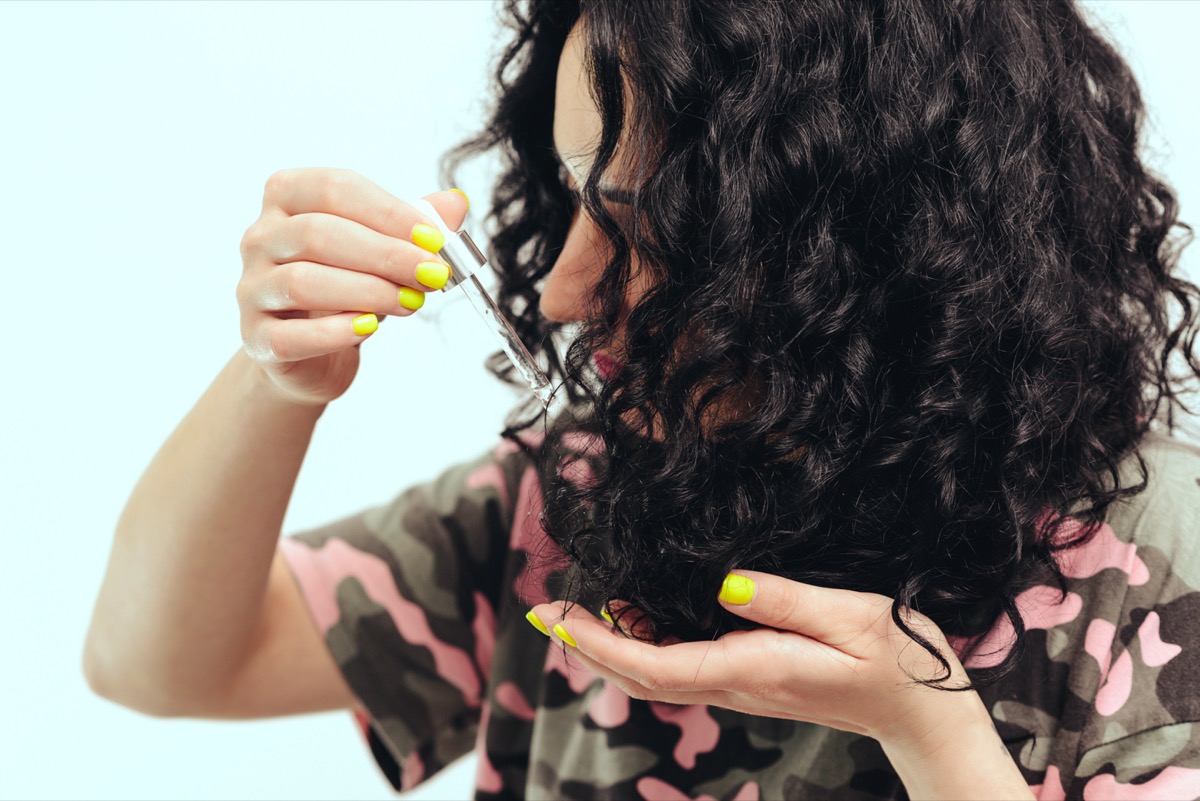 mujer joven aplicando aceite para el cabello a los rizos