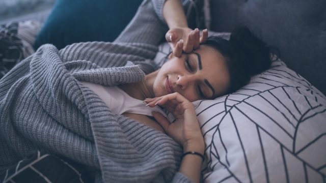 Young woman waking up at her own bed alone, with a smile