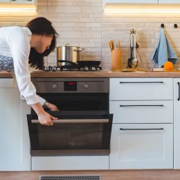 A woman wearing an apron checks inside the oven in her kitchen