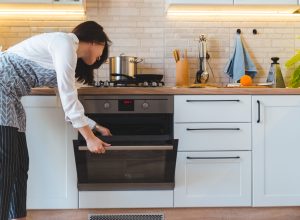 A woman wearing an apron checks inside the oven in her kitchen