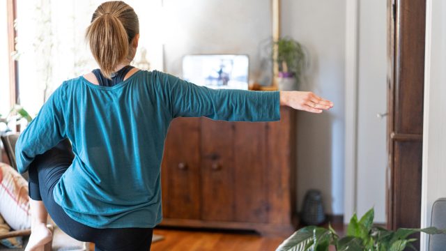 A young woman works out in her living room to a class on her laptop
