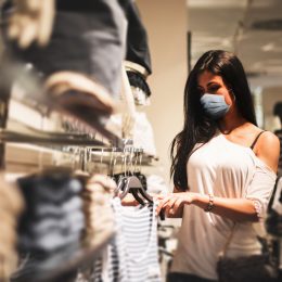 A young woman wearing a face mask shopping in a retail clothing store amid the coronavirus pandemic