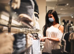 A young woman wearing a face mask shopping in a retail clothing store amid the coronavirus pandemic