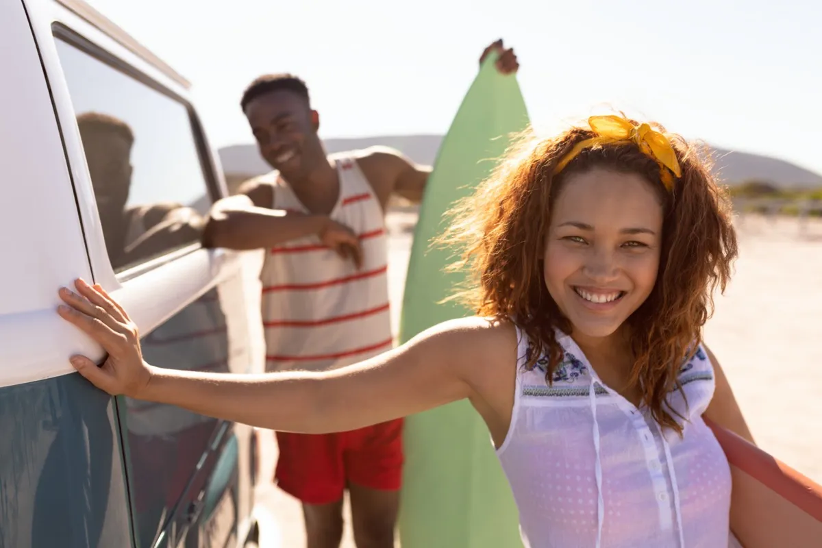 young straight black couple holding surfboards outside van