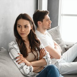 young man and woman sitting on couch arguing with arms crossed