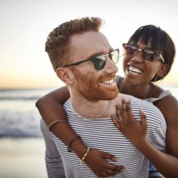 A young heterosexual couple hugging on the beach at sunset.