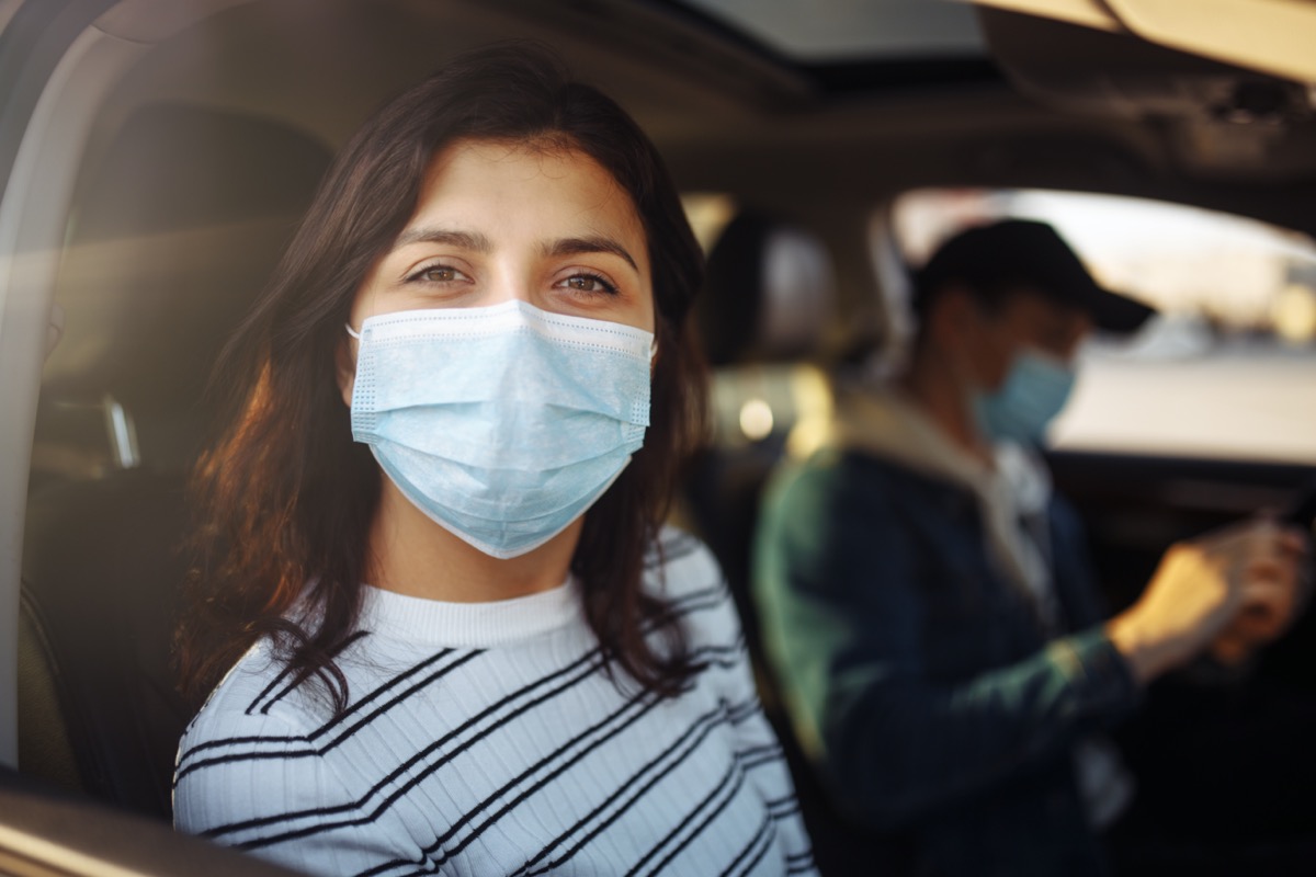 young woman wearing surgical mask in car