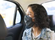 A young woman wearing a face mask in the back seat of a car