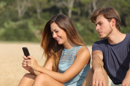 Young man looking at girlfriend's phone with jealousy
