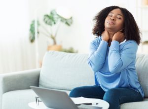 young woman sitting on couch massaging sore neck