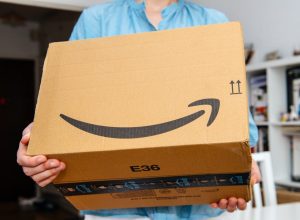 PARIS, FRANCE - JUL 4, 2018: Woman receiving Amazon Prime package delivered preparing to do the unboxing, proud Amazon Prime client with library in background