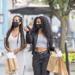 Two woman walking downtown, holding shopping bags, and doing some window shopping while wearing protective face masks during phase 2 of reopening during the COVID-19 pandemic.