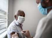 Nurse applying vaccine on patient's arm while wearing a face mask