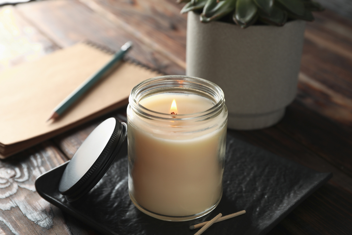 close up of burning candle in glass jar, succulent and notebook on wooden background