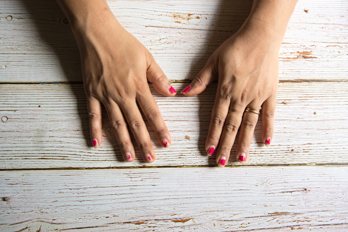 closeup of white woman's hands on wood background with chipped nail polish on fingernails