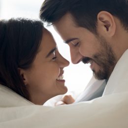 happy couple wrapped in duvet, smiling at each other