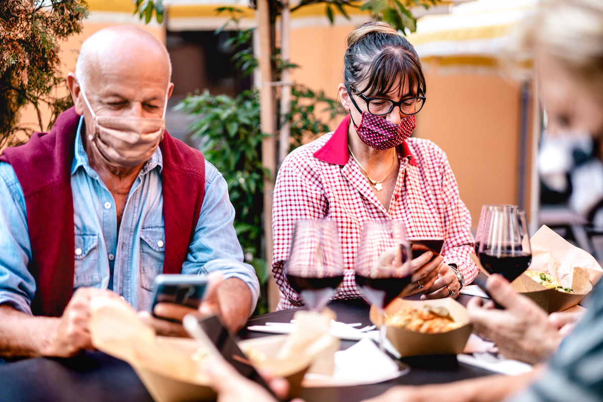 seniors at restaurant, wearing masks, having wine, and looking at their phones