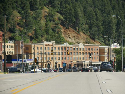 cityscape photo of shops, trees along mountains, and a road in Deadwood City, South Dakota