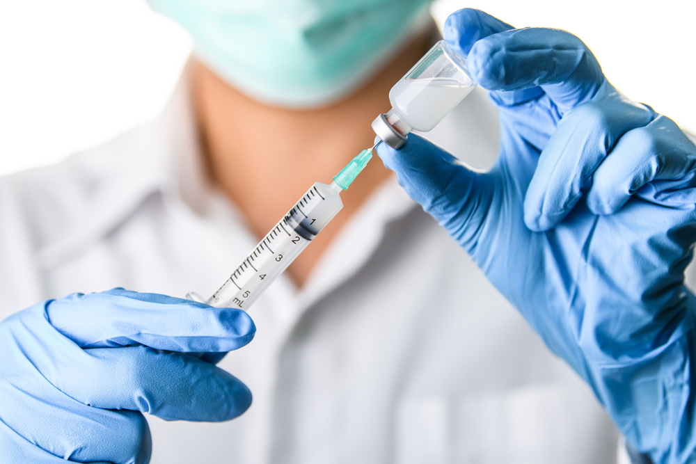 A doctor wearing blue gloves fills a syringe with COVID vaccine.