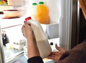 closeup of person looking at bottle of milk with open fridge door