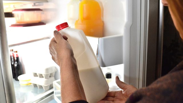 closeup of person looking at bottle of milk with open fridge door