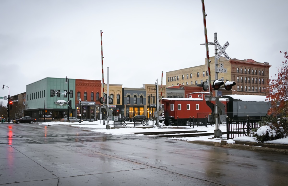 cityscape photo of shop, railroad track, and train in downtown Fargo, North Dakota in the snow