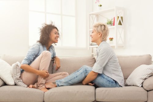 two female friends sitting on the couch and talking and smiling