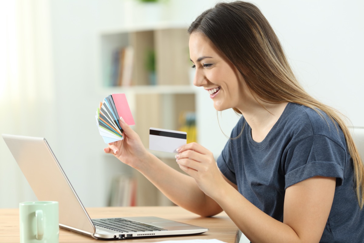 Caucasian women holding up credit cards and looking at computer while smiling