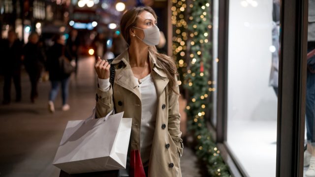 Happy woman Christmas shopping wearing a facemask and looking at a window carrying bags