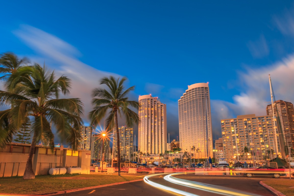 cityscape photo of palm trees, buildings, and fast moving cars in Honolulu, Hawaii