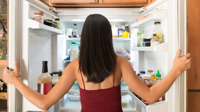 latinx woman in maroon tank top photographed from behind as she looks in the fridge