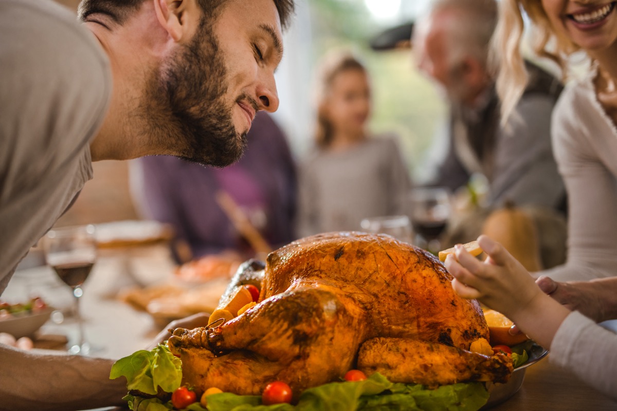 Young smiling man smelling roasted turkey on a Thanksgiving day with his family.