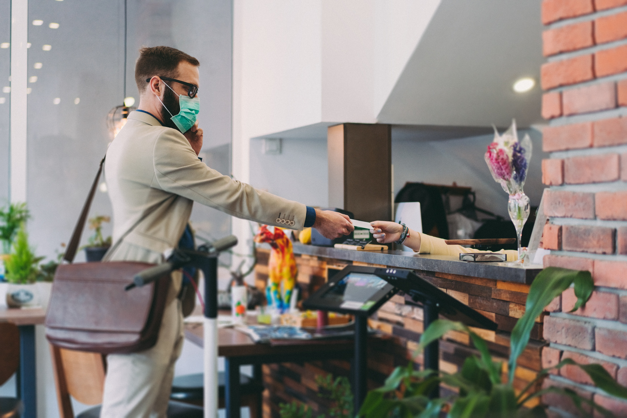 A man in a suit wearing a face mask hands over his credit card to a receptionist while checking into a hotel
