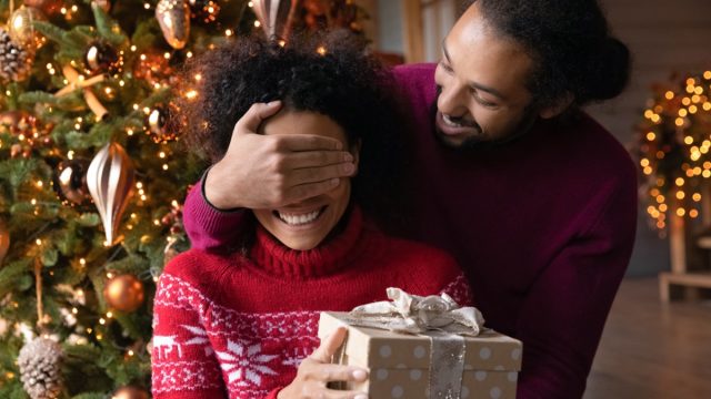 young black man giving his wife a christmas present while covering her eyes
