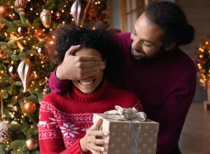 young black man giving his wife a christmas present while covering her eyes