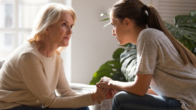 senior woman and adult daughter sitting look at each other having heart-to-heart talk, as they hold hands