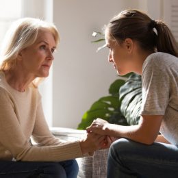 senior woman and adult daughter sitting look at each other having heart-to-heart talk, as they hold hands