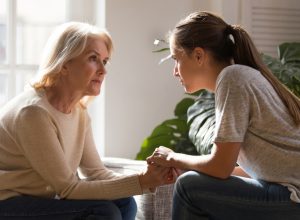 senior woman and adult daughter sitting look at each other having heart-to-heart talk, as they hold hands