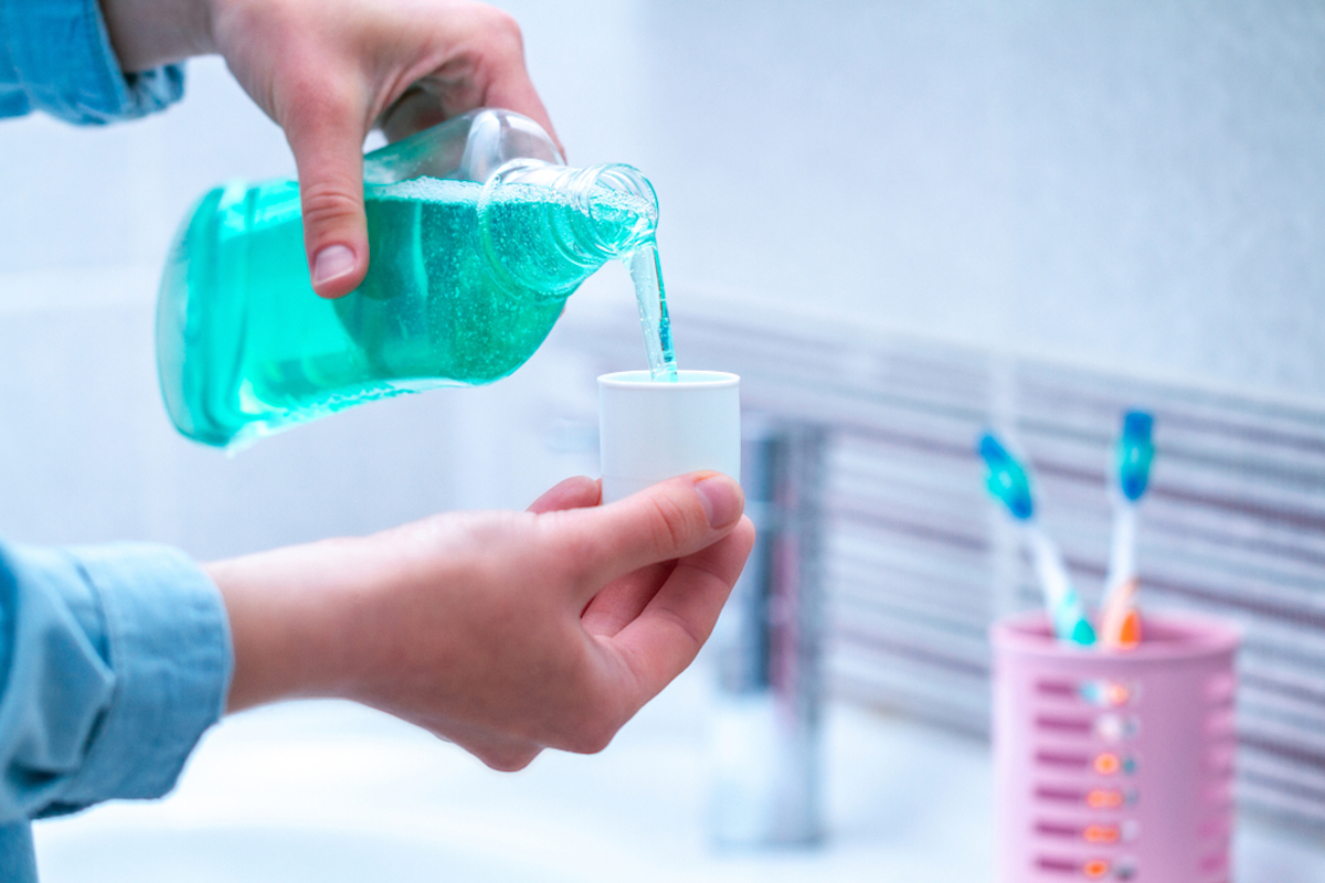 closeup of hand pouring mouth wash into cup over sink