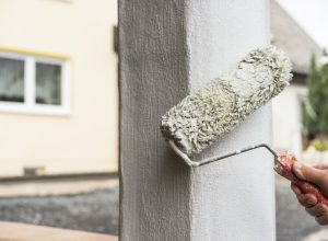 painter using roller to paint column on home's exterior