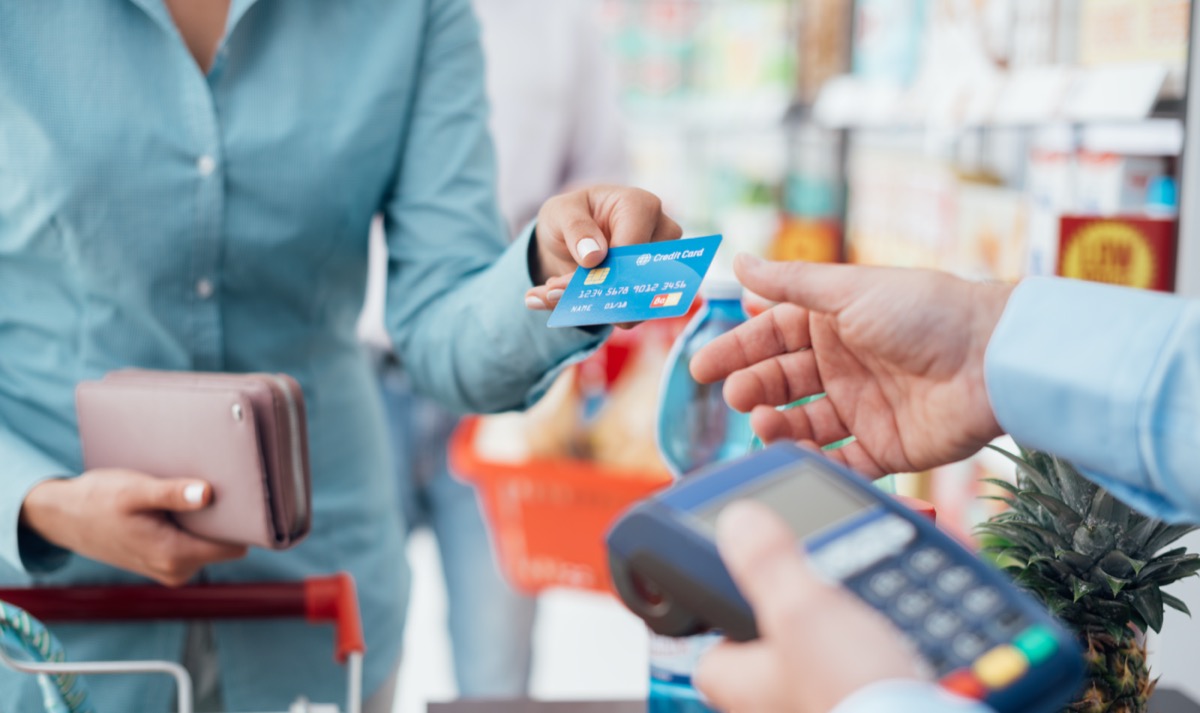 woman's hand giving a credit card to a male cashier who is holding a card reader