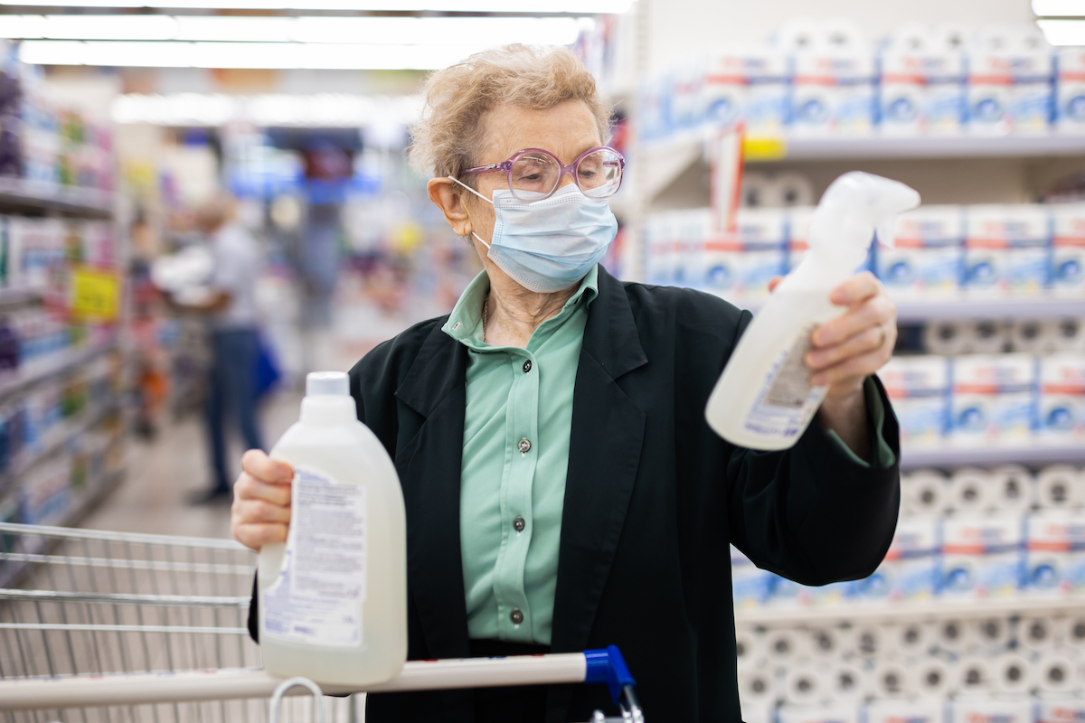 elderly woman wearing mask chooses disinfectants and detergent in household chemicals department in supermarket