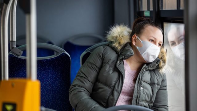 woman with face mask looking out the window on a bus