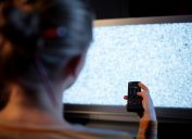 Back view of woman with remote control in front of TV set with noise on the screen