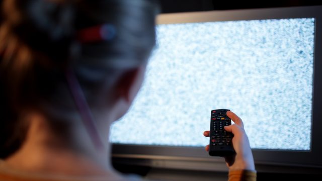 Back view of woman with remote control in front of TV set with noise on the screen
