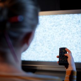 Back view of woman with remote control in front of TV set with noise on the screen