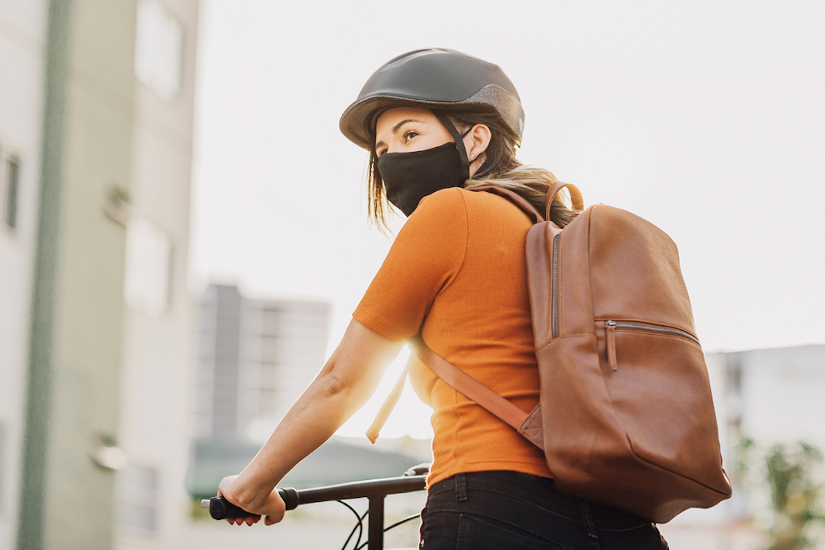 Young adult riding a bicycle through the city wearing face mask against COVID-19
